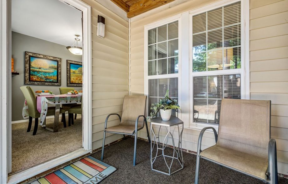 Small patio with two chairs, a side table with a potted plant, and a colorful doormat by a glass door at Madison Hunters Glen.