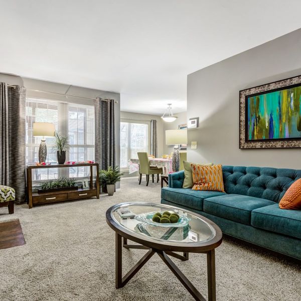 Modern living room with teal sofa, glass coffee table, large windows, and colorful wall art at Madison Hunters Glen.