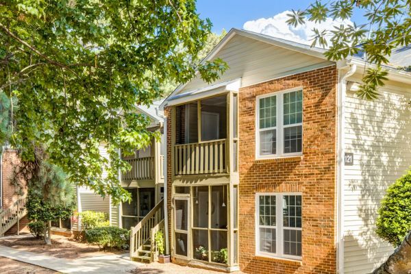 Two-story apartment building with brick and siding exterior, trees, and screened porches under a sunny sky at Madison Hunters Glen