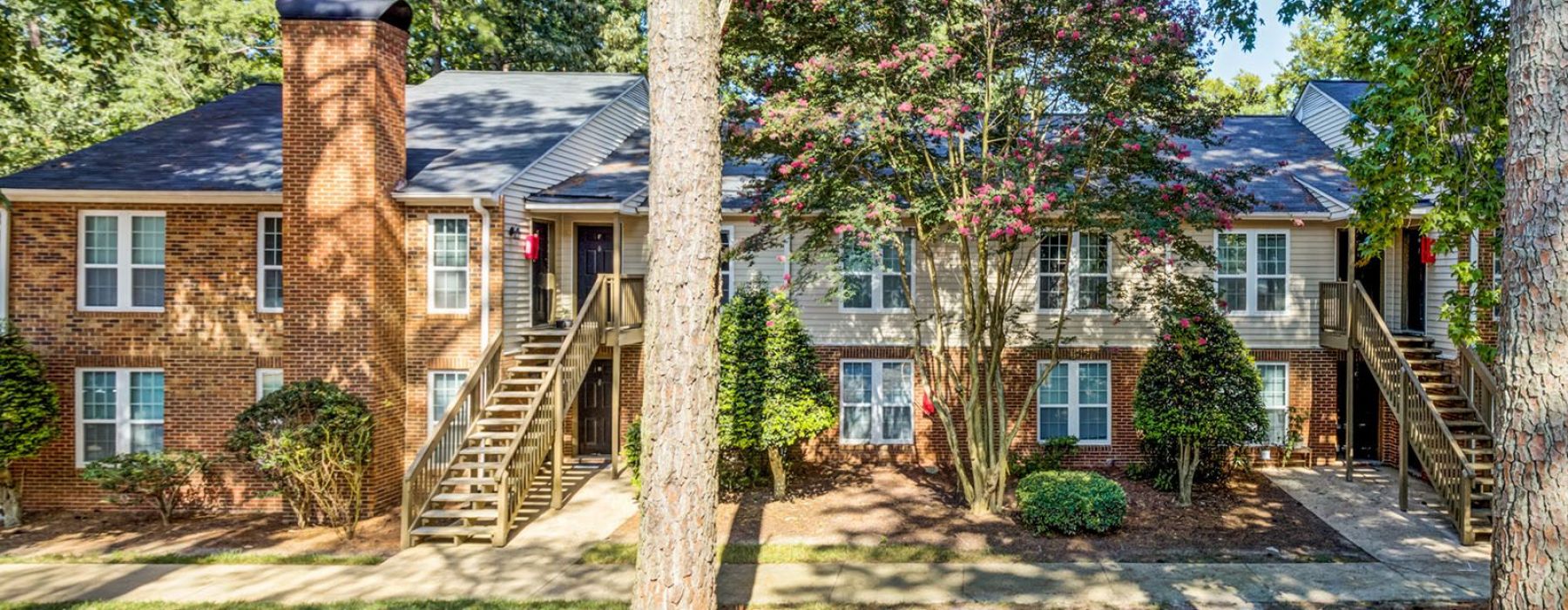 Two-story brick house with tall trees and a staircase leading to the front door, under a clear blue sky at Madison Hunters Glen