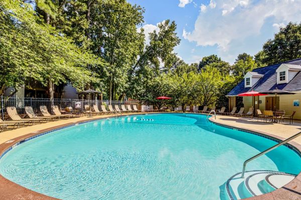 Large outdoor swimming pool surrounded by lounge chairs, trees, and buildings under a sunny sky at Madison Hunters Glen apartments.