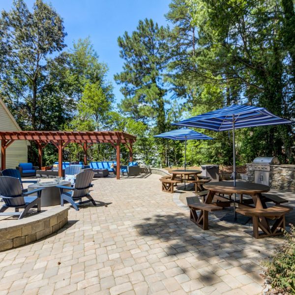 Outdoor patio with stone pavers, picnic tables under blue umbrellas, and a wooden pergola.